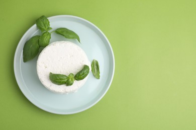 Photo of Fresh ricotta (cream cheese) and basil on green table, top view. Space for text