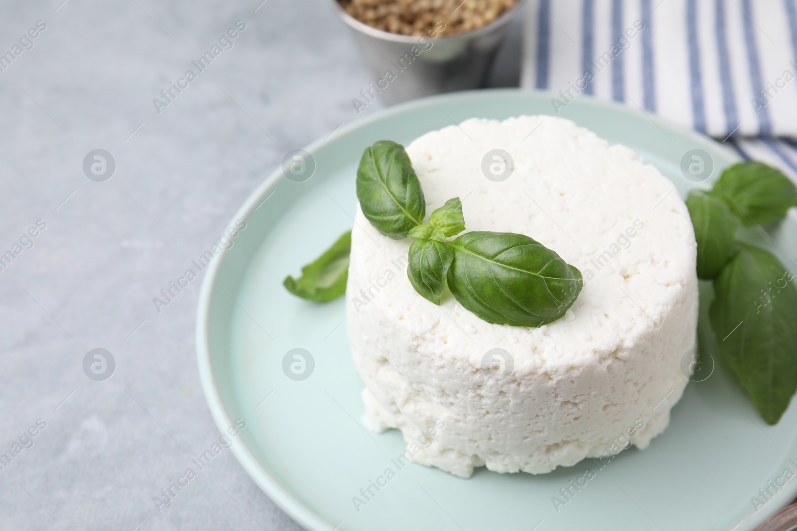 Photo of Fresh ricotta (cream cheese) and basil on gray table, closeup