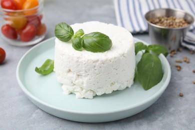 Photo of Fresh ricotta (cream cheese) and basil on gray table, closeup