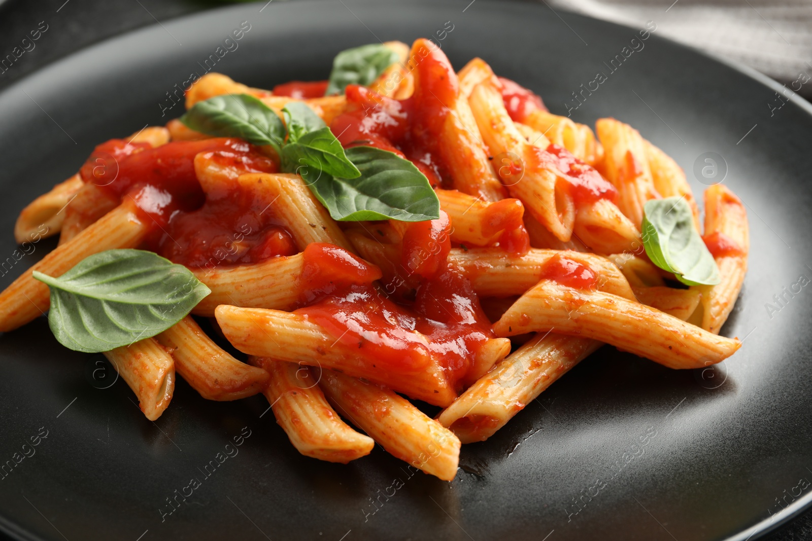 Photo of Delicious pasta with tomato sauce and basil on black plate, closeup