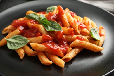 Photo of Delicious pasta with tomato sauce and basil on black plate, closeup