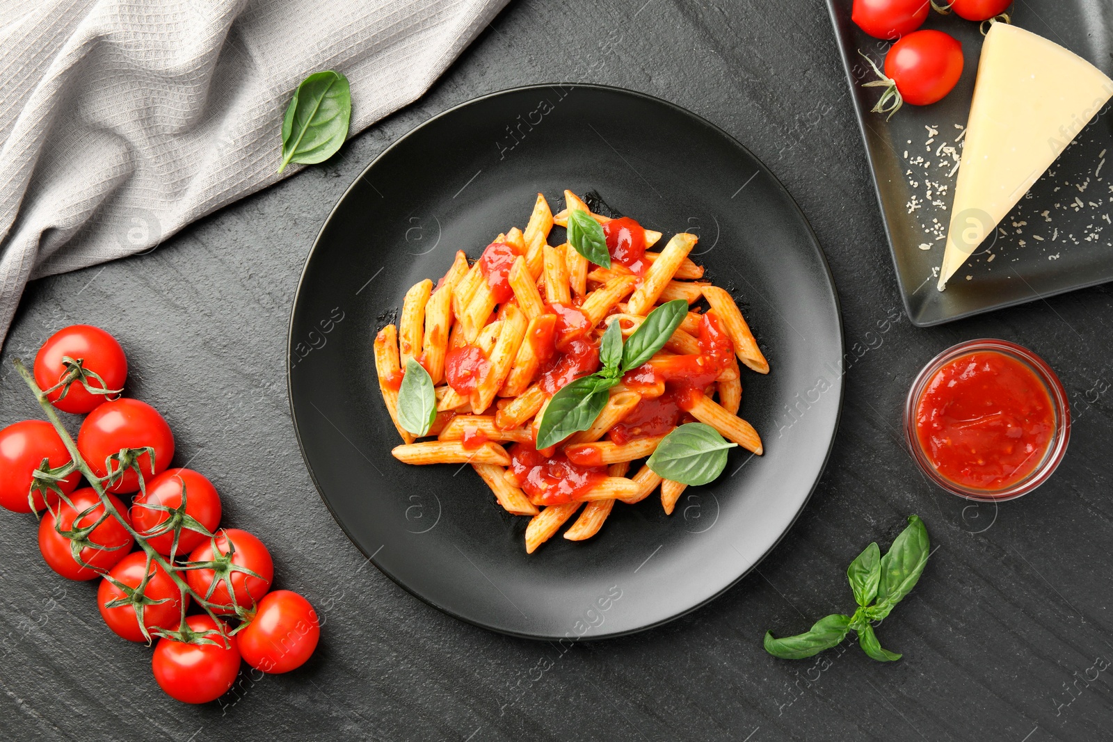 Photo of Delicious pasta with tomato sauce, basil and cheese on black textured table, flat lay