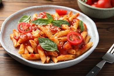 Delicious pasta with tomato sauce, basil and cheese served on wooden table, closeup