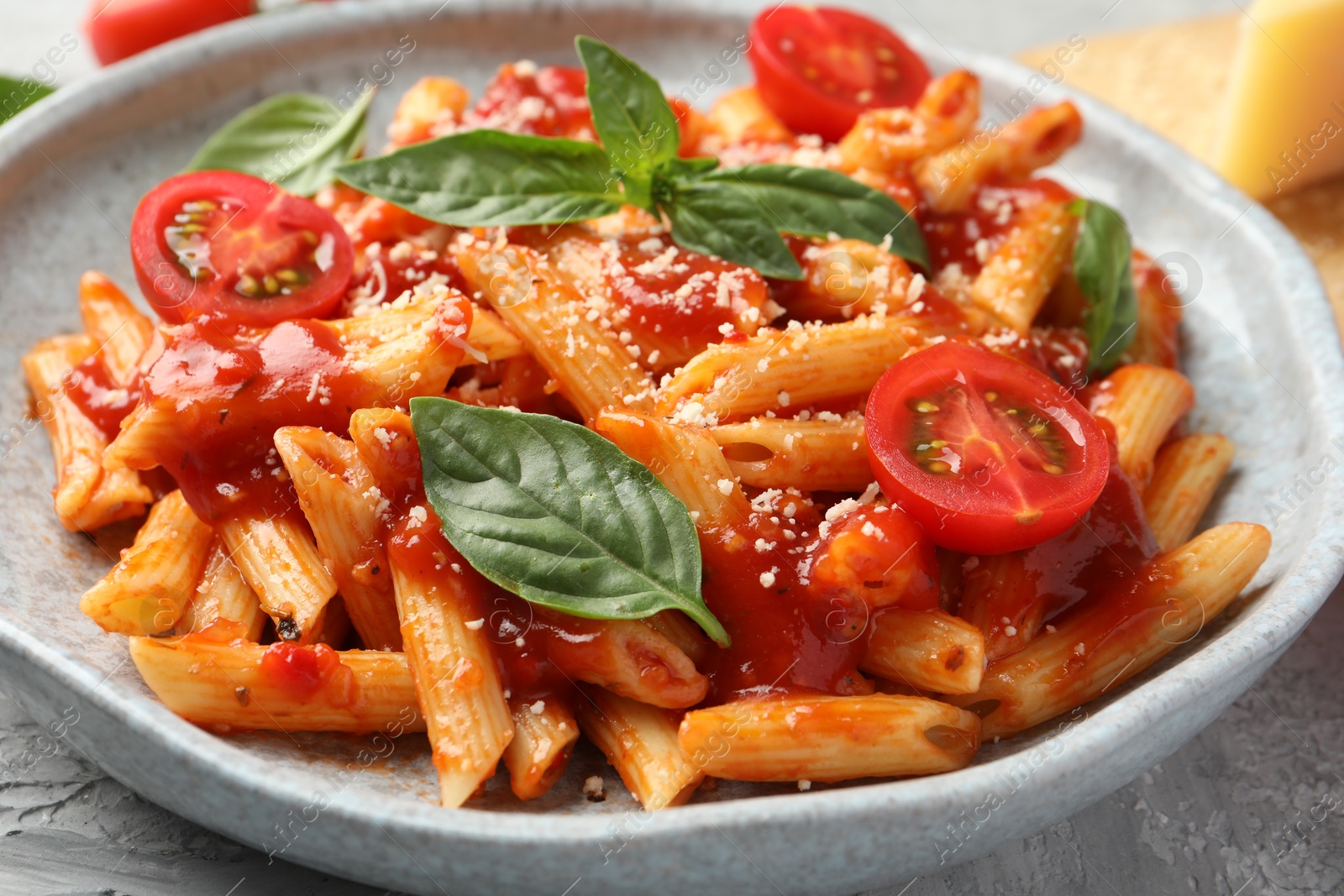 Photo of Delicious pasta with tomato sauce, basil and cheese on gray textured table, closeup