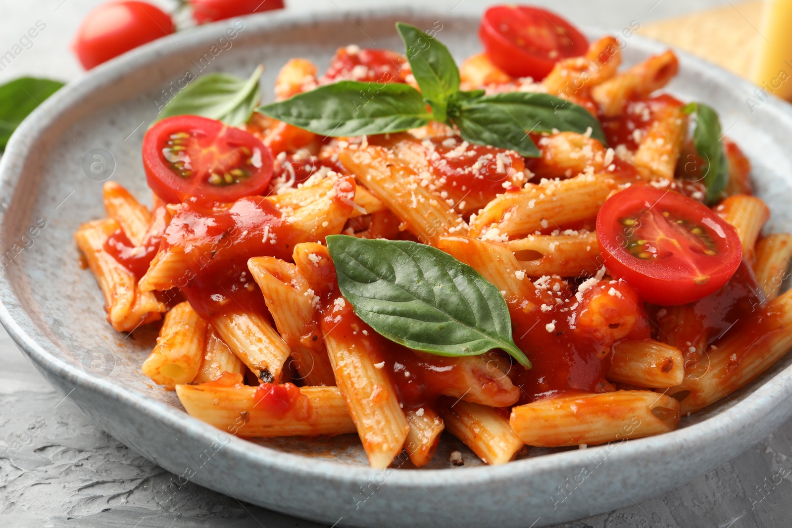 Photo of Delicious pasta with tomato sauce, basil and cheese on gray textured table, closeup