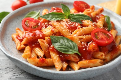 Photo of Delicious pasta with tomato sauce, basil and cheese on gray textured table, closeup