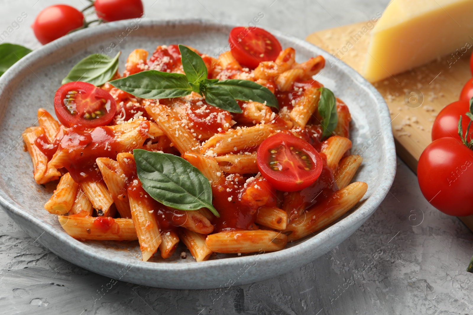 Photo of Delicious pasta with tomato sauce, basil and cheese on gray textured table, closeup