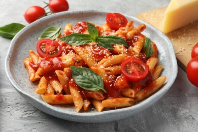 Photo of Delicious pasta with tomato sauce, basil and cheese on gray textured table, closeup