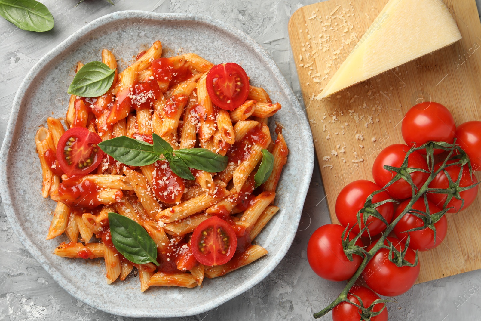 Photo of Delicious pasta with tomato sauce, basil and cheese on gray textured table, flat lay