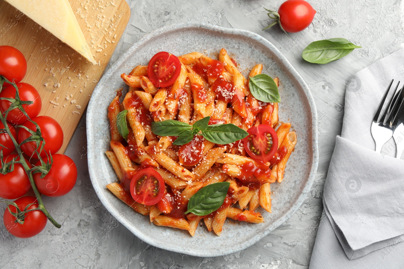 Photo of Delicious pasta with tomato sauce, basil and cheese on served gray textured table, flat lay