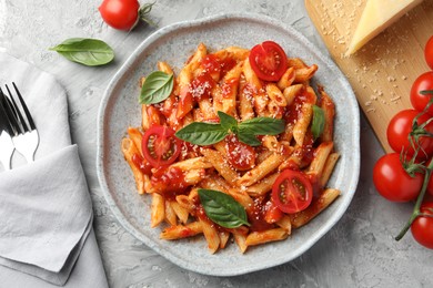 Photo of Delicious pasta with tomato sauce, basil and cheese on served gray textured table, flat lay