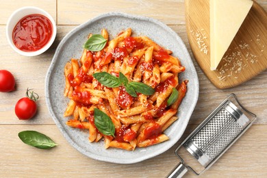 Delicious pasta with tomato sauce, basil and cheese on wooden table, flat lay