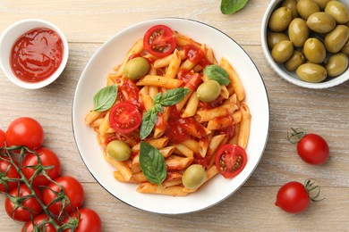 Photo of Delicious pasta with tomato sauce, basil and olives in bowl on wooden table, flat lay