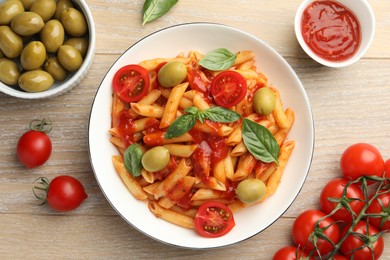 Photo of Delicious pasta with tomato sauce, basil and olives in bowl on wooden table, flat lay