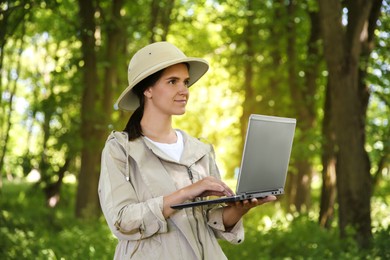 Forester with laptop examining plants in forest