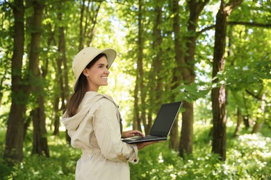 Forester with laptop examining plants in forest, space for text