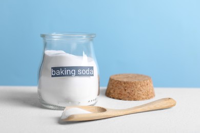 Photo of Baking soda in glass jar and spoon on white table