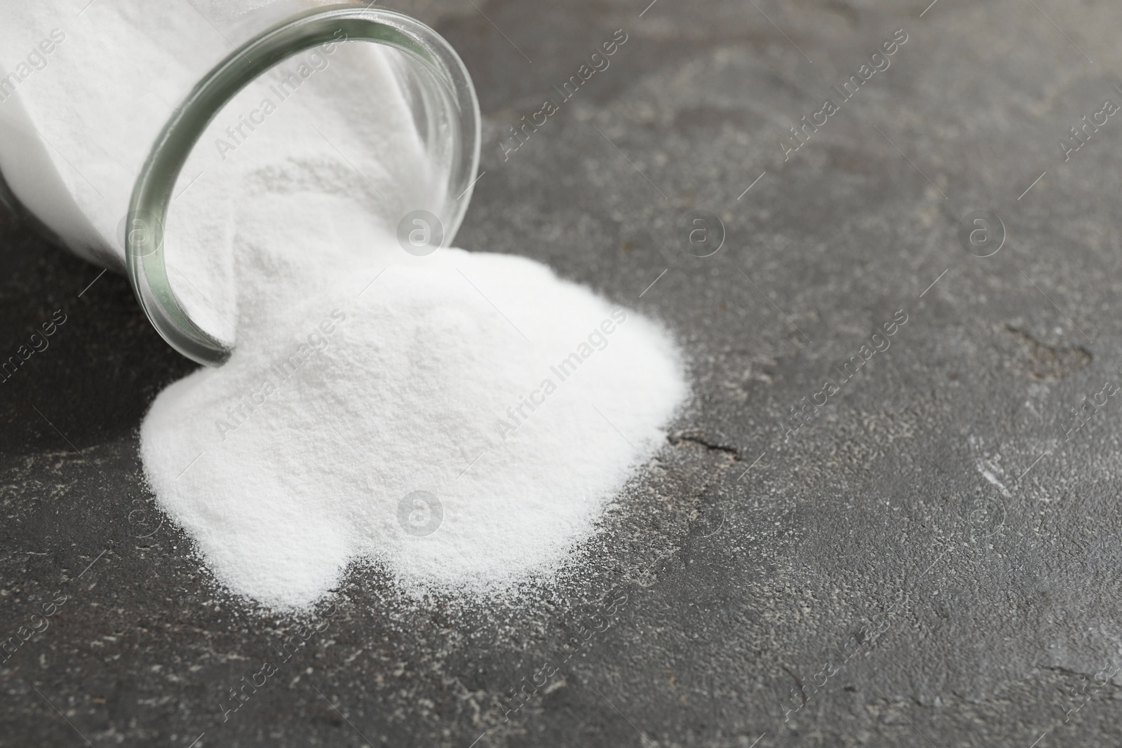 Photo of Baking soda in glass jar on grey table, closeup. Space for text