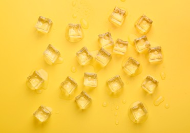 Crystal clear ice cubes on yellow background, flat lay