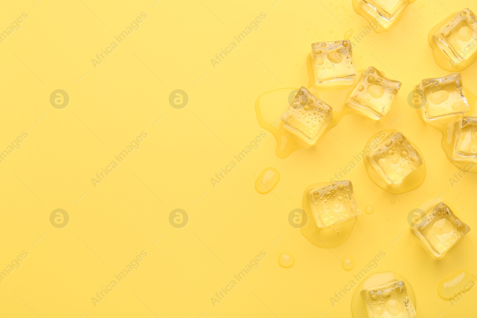 Photo of Crystal clear ice cubes on yellow background, flat lay. Space for text