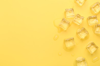 Crystal clear ice cubes on yellow background, flat lay. Space for text