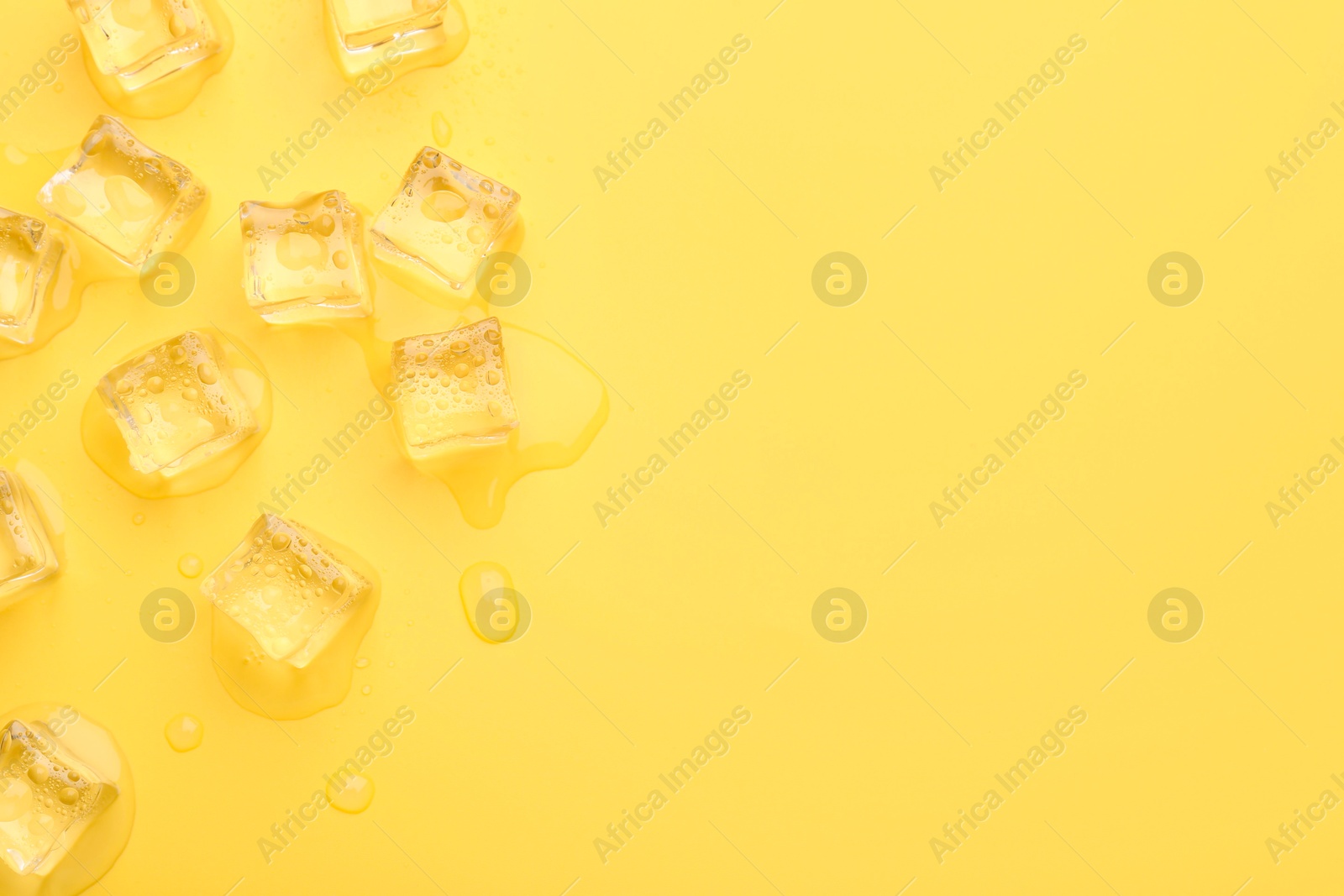 Photo of Crystal clear ice cubes on yellow background, flat lay. Space for text