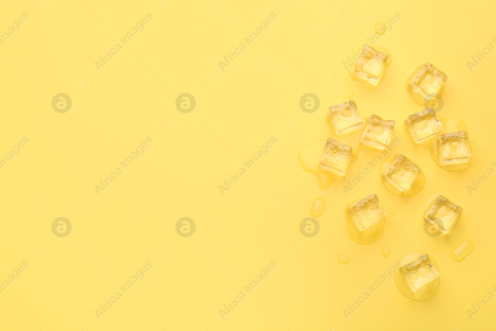 Photo of Crystal clear ice cubes on yellow background, flat lay. Space for text