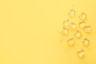 Photo of Crystal clear ice cubes on yellow background, flat lay. Space for text