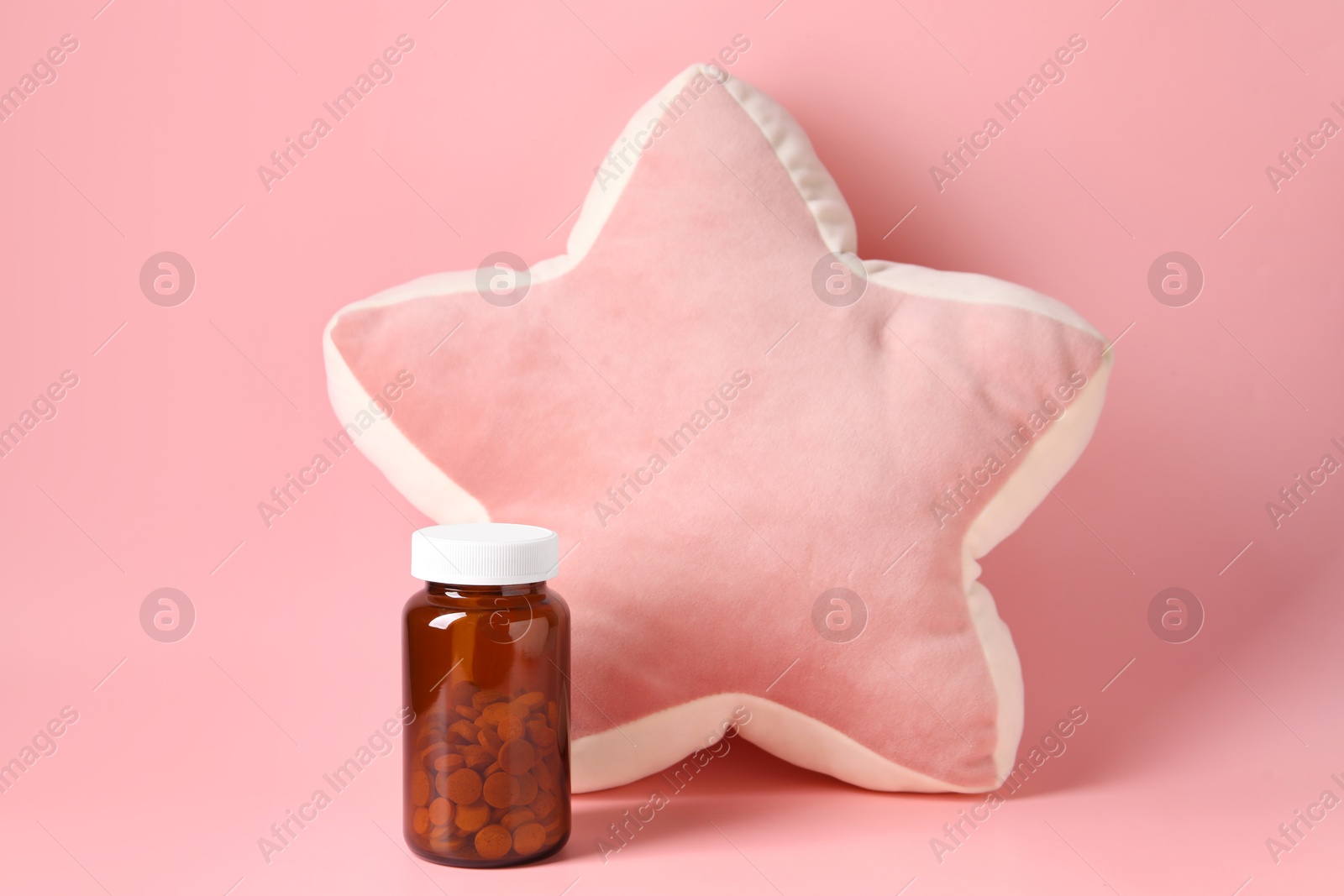Photo of Star shaped pillow and bottle of pills on pink background