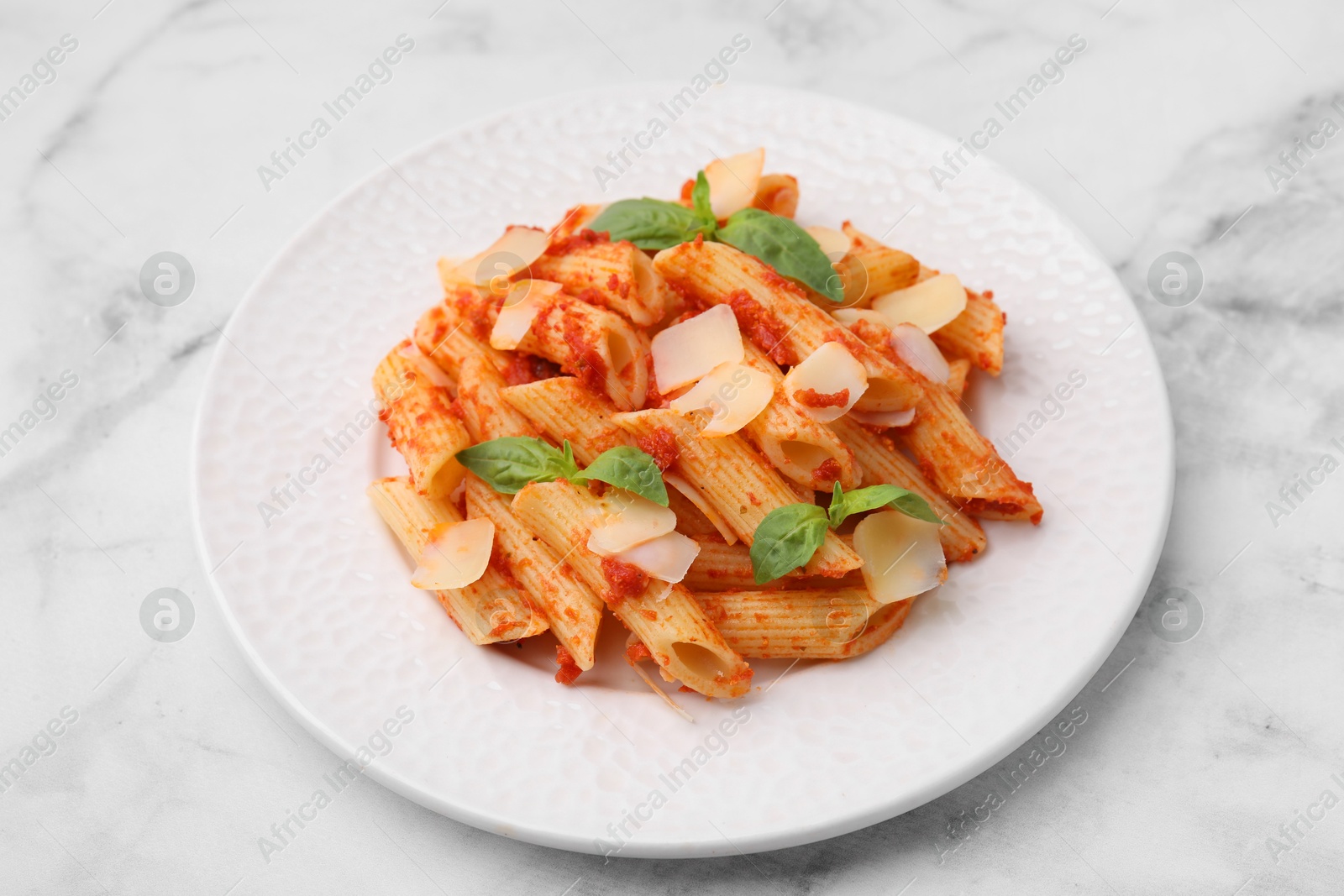 Photo of Tasty pasta with tomato sauce, cheese and basil on white marble table