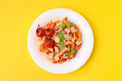 Tasty pasta with tomato sauce, cheese and basil on yellow background, top view