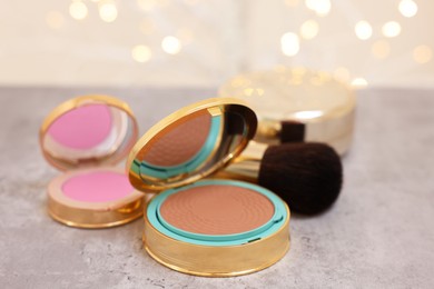 Photo of Face bronzer, blusher and makeup brush on grey textured table against blurred lights, closeup