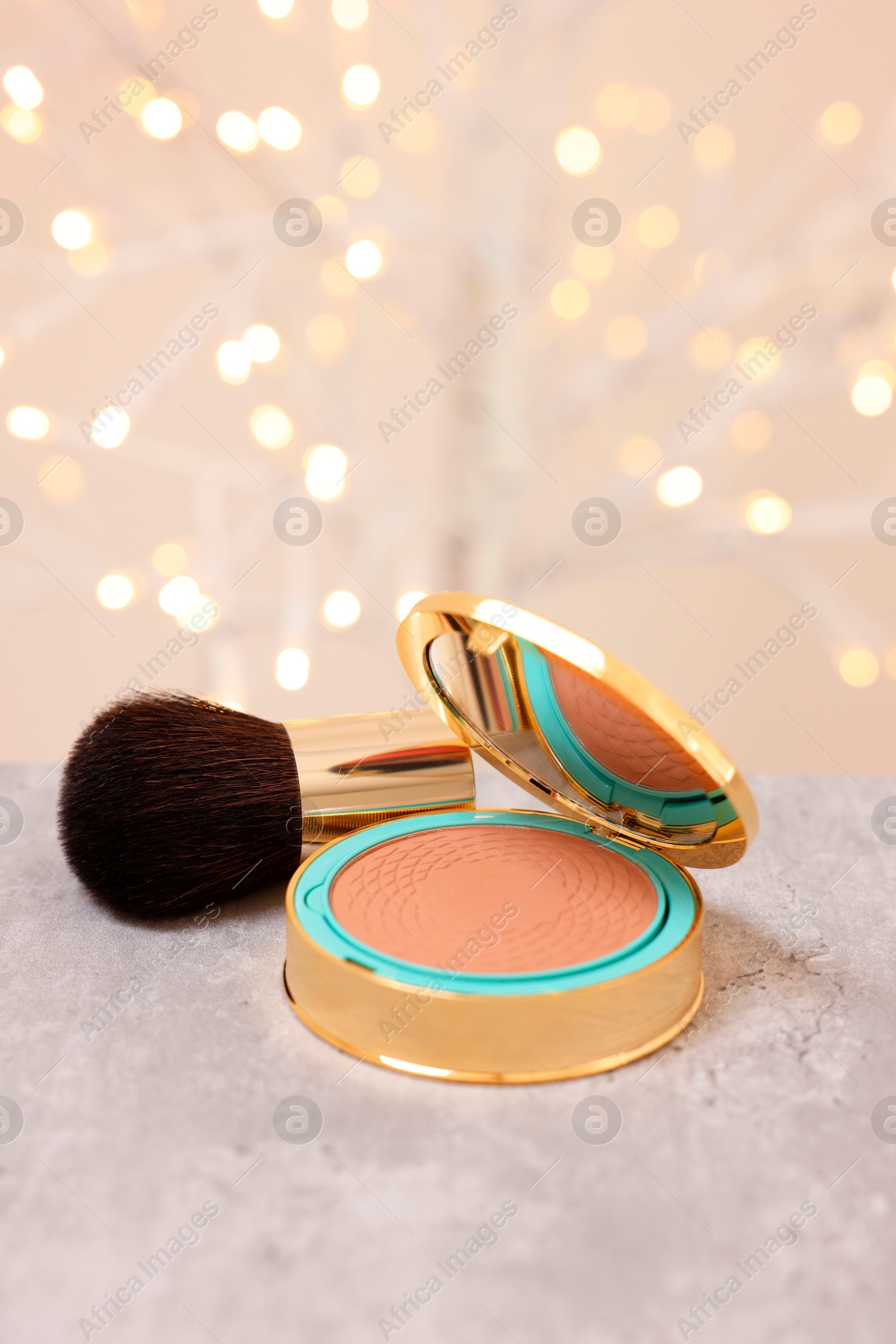 Photo of Face bronzer on grey textured table against blurred lights. Space for text