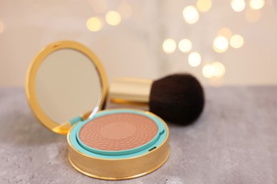 Face bronzer on grey textured table against blurred lights, closeup