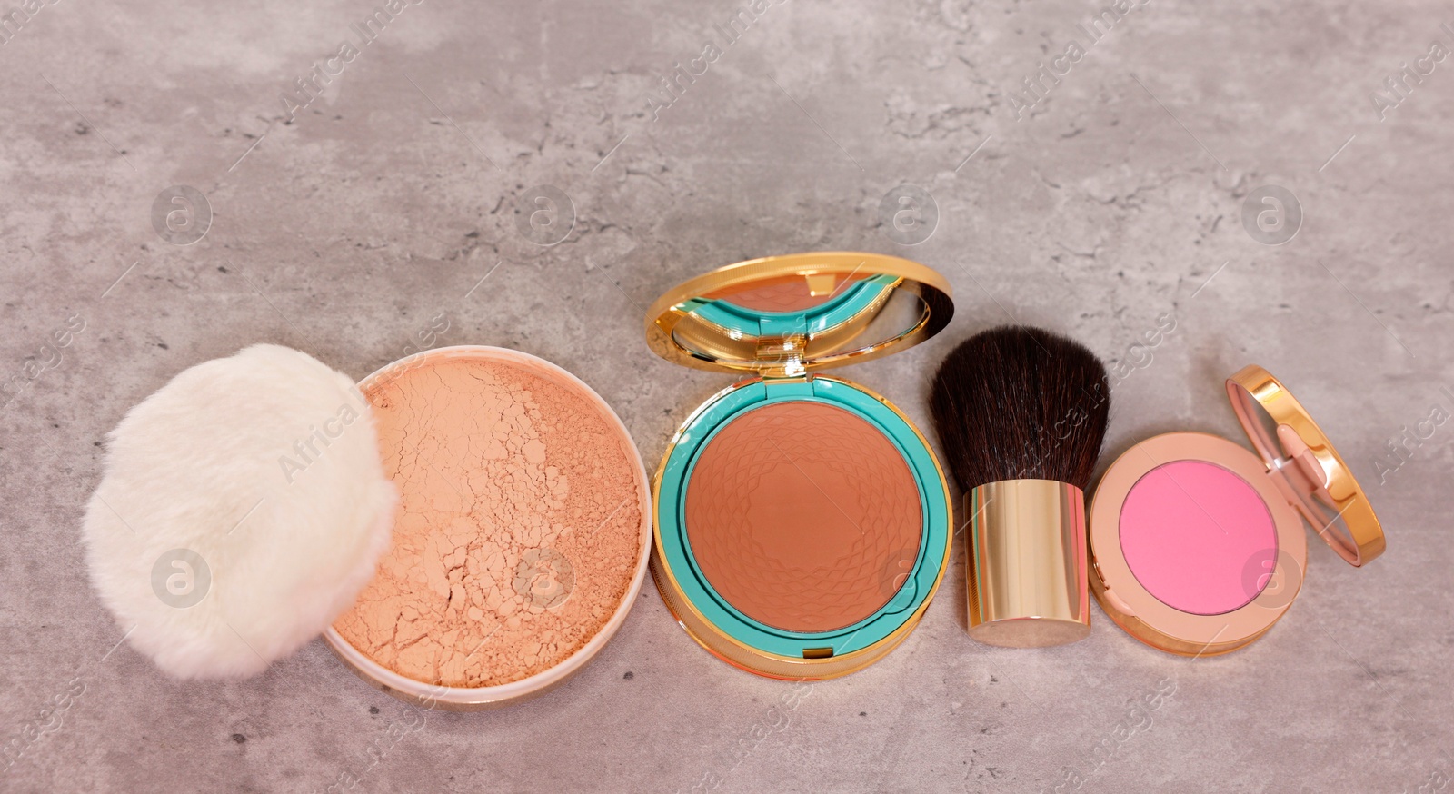 Photo of Bronzer, powder, blusher and brush on grey textured table, above view. Space for text