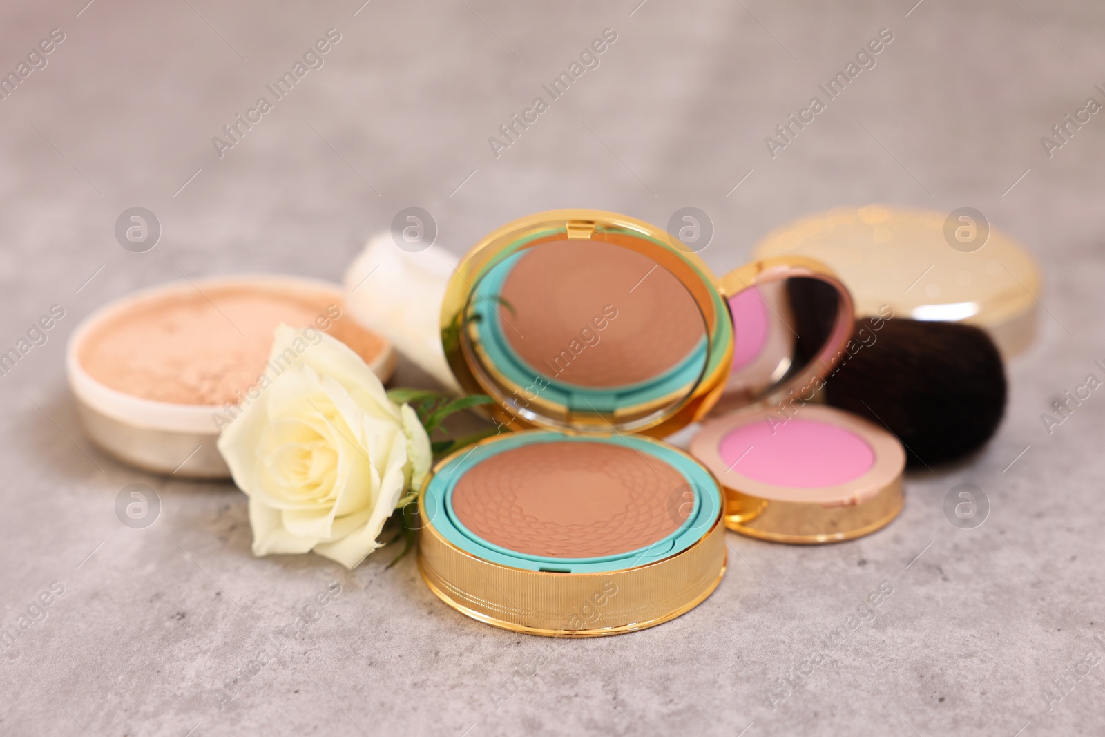 Photo of Composition with bronzer, blusher and rose flower on grey textured table, closeup