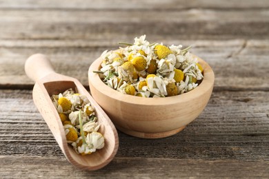 Photo of Chamomile flowers in bowl and scoop on wooden table, closeup