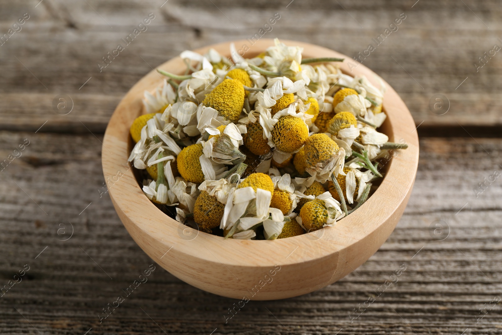 Photo of Chamomile flowers in bowl on wooden table, closeup