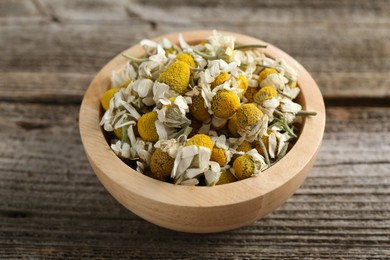 Photo of Chamomile flowers in bowl on wooden table, closeup