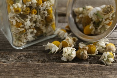 Chamomile flowers in glass jar and sieve on wooden table, closeup