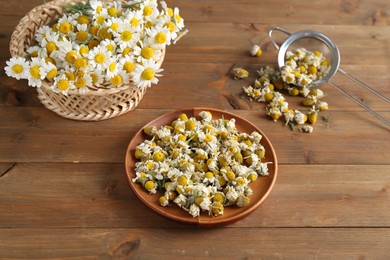 Photo of Dry and fresh chamomile flowers on wooden table