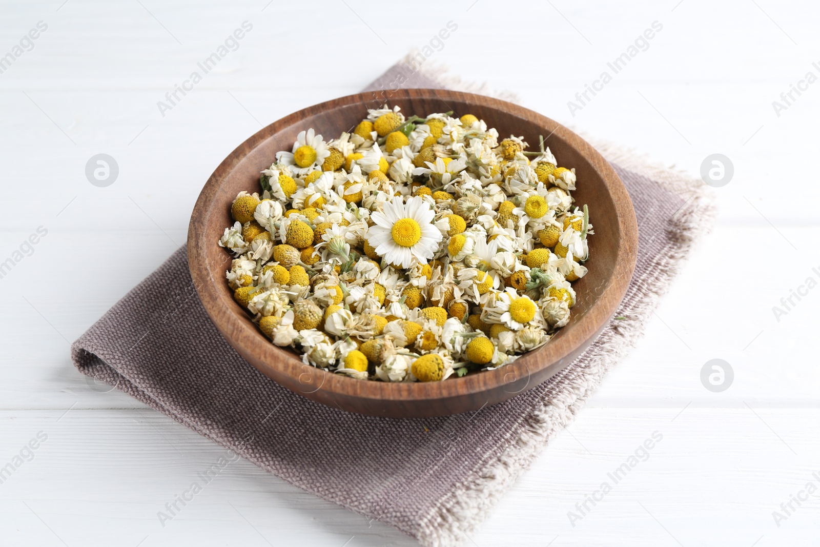 Photo of Dry and fresh chamomile flowers in bowl on white wooden table