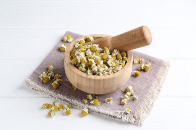 Photo of Mortar and pestle with chamomile flowers on white wooden table