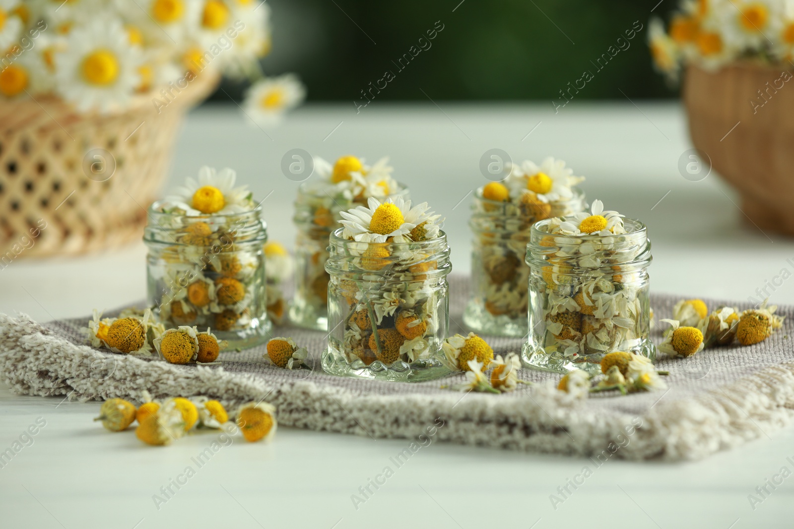 Photo of Dry and fresh chamomile flowers in glass jars on light table, closeup