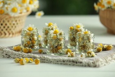 Dry and fresh chamomile flowers in glass jars on light table, closeup