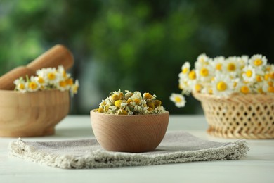 Chamomile flowers in bowl on light table against blurred green background