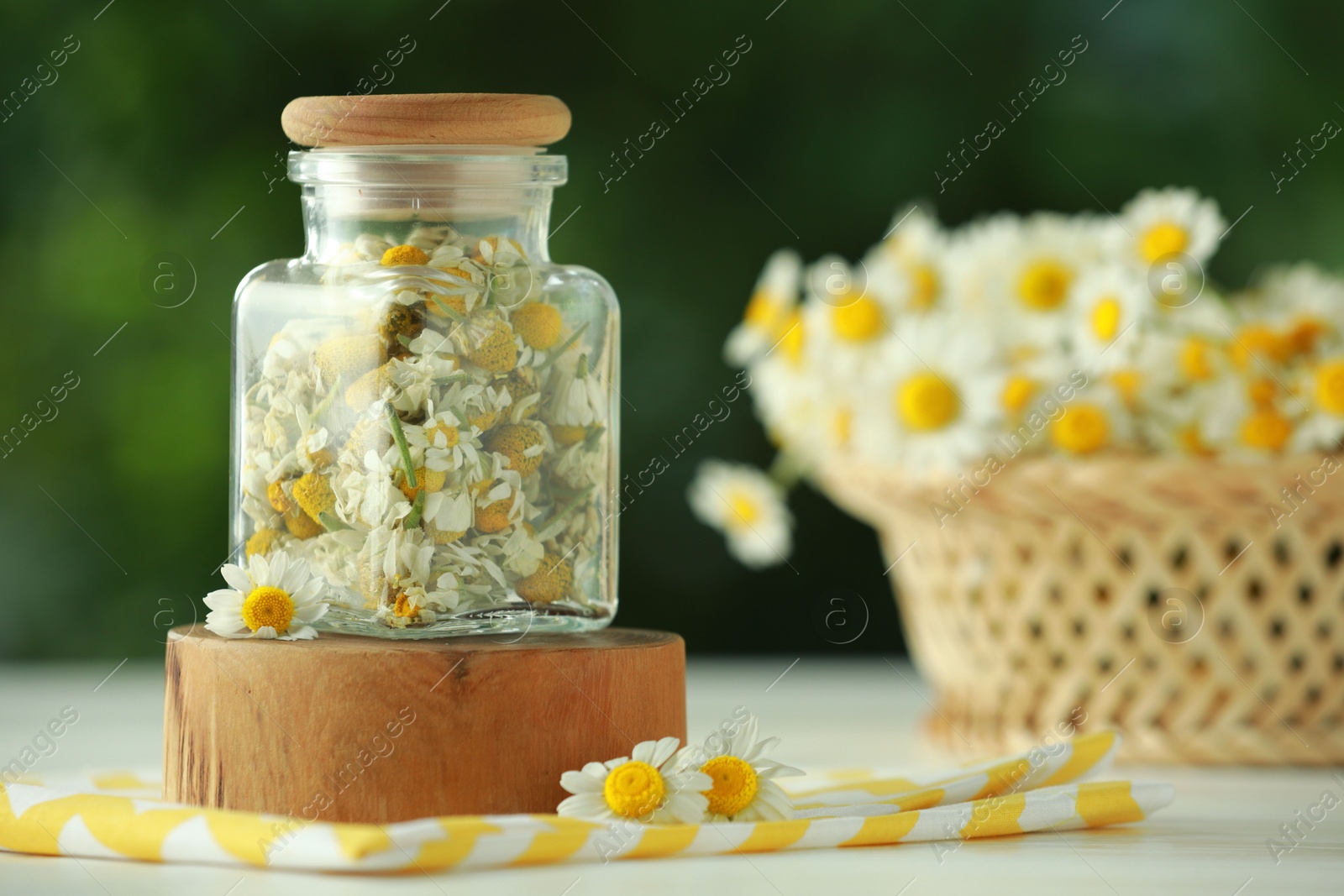 Photo of Dry and fresh chamomile flowers in glass jar on light table against blurred green background