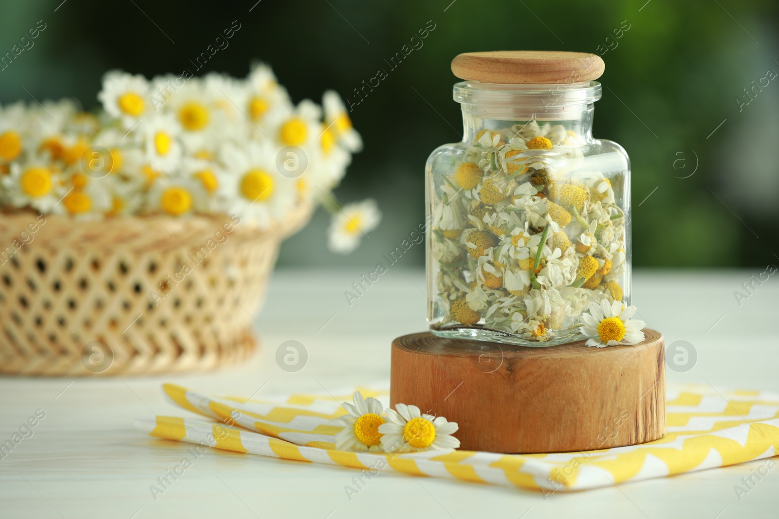 Photo of Dry and fresh chamomile flowers in glass jar on light table against blurred green background