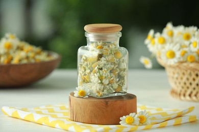 Photo of Dry and fresh chamomile flowers in glass jar on light table against blurred green background