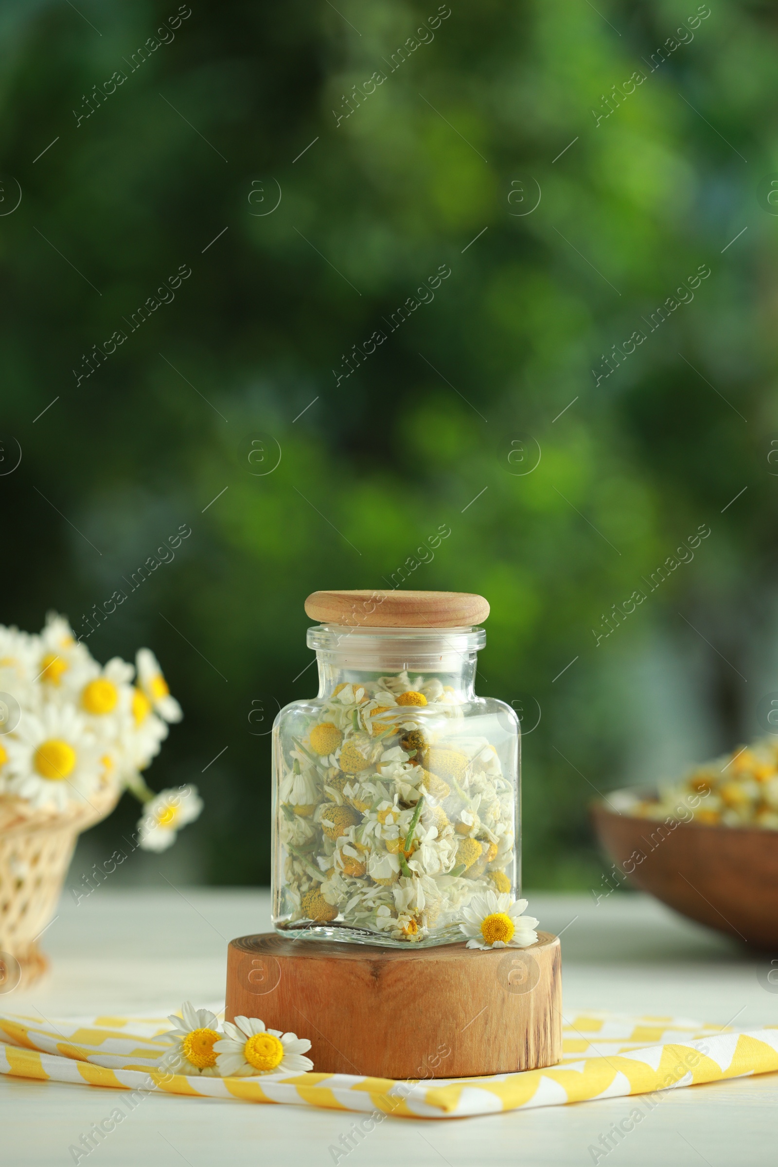 Photo of Dry and fresh chamomile flowers in glass jar on light table against blurred green background, space for text